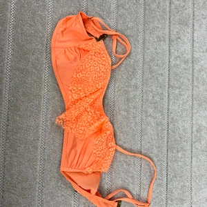 Korallfärgad bikiniöverdel med spets från KappAhl - Säljer en snygg korallfärgad bikiniöverdel från KappAhl i storlek XS. Bikinin har spetsdetaljer framtill, justerbara axelband och knäppning bak. Perfekt för stranden eller poolen!