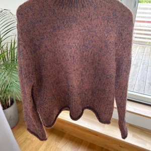 Stickad tröja med glittertråd från Moves - Säljer en brun stickad tröja från Moves i storlek XS. Tröjan har inslag av blå glittertråd som ger en snygg effekt. Den har lång ärm och hög krage, perfekt för kyliga dagar. Knappt använd!