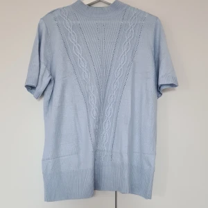 Ljusblå stickad kortärmad tröja från Established - Säljer en ljusblå stickad tröja från Established med korta ärmar och diskret kabelstickat mönster framtill. Tröjan har ribbade muddar och hög hals, perfekt för en stilren look.