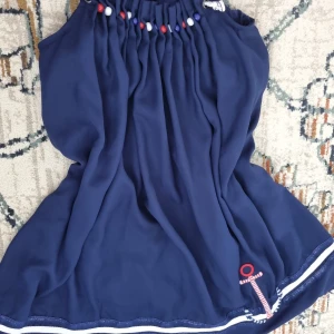 Marinblå klänning med pärldetaljer från Desigual - Söt marinblå klänning från Desigual med pärlor i rött, vitt och blått vid halsen samt ett ankare och randiga band längst ner. Perfekt för sommarens alla tillfällen.