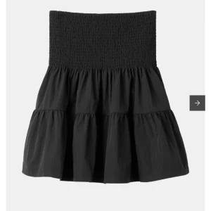 Svart volangkjol från Carin Wester - Supersnygg svart kjol från Carin Wester med bred smock i midjan och flera volanger. Kjolen är kort och har en luftig känsla, perfekt att styla med en enkel topp eller hoodie. Bara använd en gång! Storlek L och är dom en M/L
