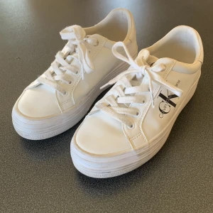 Vita sneakers från Calvin Klein Jeans - Snygga vita sneakers från Calvin Klein Jeans med klassisk design och svart logga på sidan. Skorna är använda 3 gånger av mig och 1 gång av den jag köpte. Säljer dessa då dom var för små i storlek, riktigt sköna annars. Dessa kostar även 1200 nya