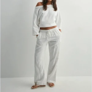 Vita linnebyxor med dragsko - Säljer ett par vita linnebyxor med avslappnad passform och dragsko i midjan. Byxorna har raka, vida ben och sidofickor. Perfekta för varma dagar och enkel stil.