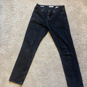 Svarta jeans från Jack & Jones - Säljer ett par svarta jeans från Jack & Jones med klassisk femficksdesign och raka ben. Jeansen har normal passform och är tillverkade i bomull. Perfekta för dig som gillar stilrena och enkla byxor.