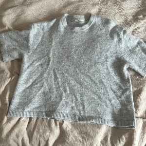 Ljusgrå stickad tröja från Gina Tricot - Mysig ljusgrå stickad tröja från Gina Tricot i storlek M. Tröjan har korta ärmar, rund halsringning och en avslappnad passform. Perfekt för lager-på-lager eller som en enkel bas i garderoben.