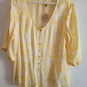 Gul blommig blus från Odd Molly - Superfin blommig blus från Odd Molly i vintagegul färg. Blusen har v-ringning, knappar framtill och trekvartsärm. Perfekt för dig som gillar ljusa och somriga plagg med fina detaljer.
