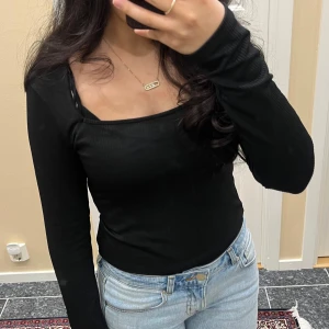 Svart ribbad långärmad topp - Säljer en svart ribbad långärmad topp med fyrkantig ringning. Sitter tight och är perfekt att styla med jeans eller kjol. Enkel och stilren design som passar till många tillfällen.