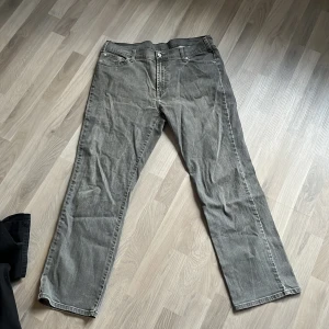 Grå jeansbyxor med raka ben - Säljer ett par grå jeansbyxor med klassisk femficksdesign och raka ben. Byxorna har normal passform och stängs med dragkedja och knapp. Perfekta för dig som gillar en enkel och tidlös stil. Storlek 40/32