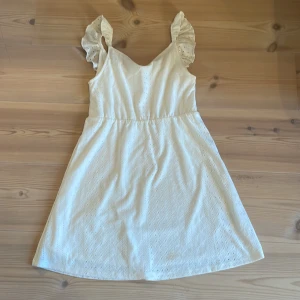Vit klänning med volangärmar från H&M - Söt vit klänning från H&M med volangärmar och broderade detaljer. Klänningen har en lätt A-linjeform och är ärmlös med fina spetsinslag. Perfekt för sommarens alla tillfällen. Står att den är i storlek 146/152 men är väldigt kort så kan vara mindre storlek. 
