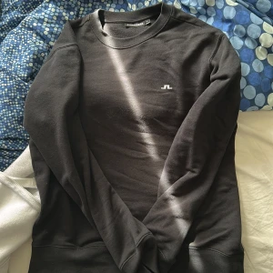  crewneck J.Lindeberg - Säljer en svart sweatshirt från J.Lindeberg med diskret logga på bröstet. Tröjan har rund halsringning och långa ärmar. Perfekt för en stilren och enkel look.