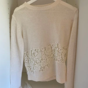 Vit stickad tröja med spetsdetalj - Säljer en vit stickad tröja med lång ärm och vacker spetsdetalj i blommigt mönster runt midjan. Perfekt för dig som gillar romantiska och feminina detaljer. Tröjan har rund halsringning och är mjuk och bekväm. Den har en minimalistisk fläck men den går bort i tvätten. Köpt från Zara men säljs inte längre