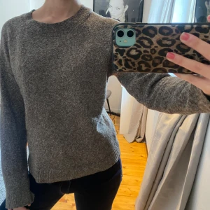 Grå stickad tröja med rund hals - Mysig grå stickad tröja med rund hals och långa ärmar. Perfekt för kyligare dagar och enkel att matcha med olika outfits. Klassisk och stilren design.