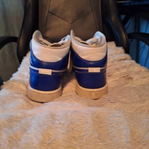 Nike Air Jordans blå och vita - Säljer ett par klassiska Nike Air Jordans i blått och vitt. Skorna har högt skaft, snörning och rund tå. Perfekta för dig som gillar streetwear och vill sticka ut med en ikonisk sneaker.