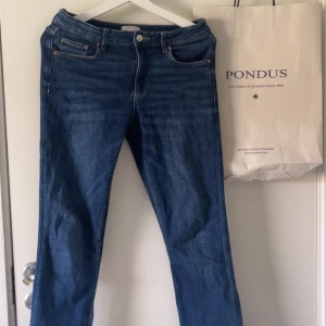 Blå jeansbyxor med utsvängd passform - Säljer ett par klassiska blå jeansbyxor med fem fickor och utsvängd passform. Byxorna har låg midja och stängs med dragkedja och knapp. Perfekta till vardags och enkla att matcha med olika toppar. Använd fåtal gånger.