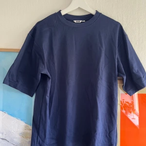 Mörkblå t-shirt från Uniqlo U - Säljer en stilren mörkblå t-shirt från Uniqlo U i storlek M. T-shirten har klassisk passform, rund halsringning och är tillverkad i mjuk bomull. Perfekt basplagg för garderoben. T-shirten är använd 2 ggr och i inprincip nyskick.
