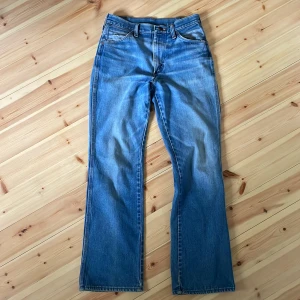 Blå vintagejeansbyxor från Wrangler - Klassiska blå jeans från Wrangler med raka ben och normal passform, lite bootcut i slutet men inte mycket. Byxorna har fem fickor, bälteshällor och en brun läderpatch med Wrangler-logga bak. Perfekta för en avslappnad stil. Lite snygga slitningar syns på jeansen. Midja är mellan 29 och 30 men passar båda. Skriv om du undrar något :)