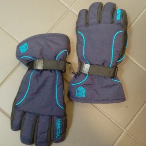 Blå vinterhandskar från Hestra - Mörkblå vinterhandskar från Hestra med svarta handflator och turkosa detaljer. Handskarna har justerbart spänne vid handleden och är fodrade för extra värme. Perfekta för kalla dagar.