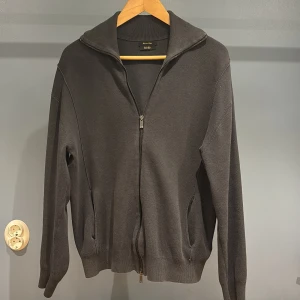 Mörkgrå ziptröja från Massimo Dutti - Säljer en stilren mörkgrå fullzip från Massimo Dutti i extra fin bomull. Tröjan har hel dragkedja, hög krage och två fickor framtill. Perfekt för lager-på-lager och enkel att matcha med det mesta.