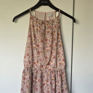 Blommig sommarklänning från Lindex - Söt blommig klänning från Lindex i ljusrosa med gula, rosa och gröna detaljer. Klänningen är ärmlös, har volang nertill och ett luftigt fall