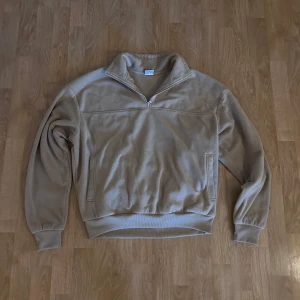 Beige fleece half zip från Urban Classics - Säljer en beige fleece-tröja från Urban Classics i storlek M. Tröjan har half zip, hög krage och långa ärmar med muddar. Perfekt för kyliga dagar och enkel att matcha med jeans eller mjukisbyxor.