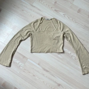 Beige croppad långärmad topp NA-KD - Trendig croppad topp från NA-KD i beige färg. Modellen har långa ärmar med lätt utsvängd form och en stilren, enkel design. Perfekt att matcha med höga jeans eller kjol för en snygg look.