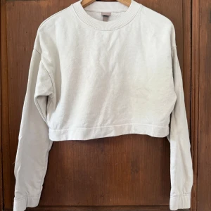 Vit croppad sweatshirt från H&M - Säljer en stilren vit croppad sweatshirt från H&M. Tröjan har rund halsringning, långa ärmar och är tillverkad i mjuk bomull. 