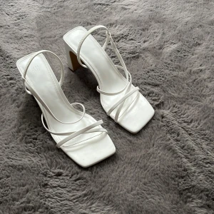 Vita sandaler med klack från H&M - Stilrena vita sandaler från H&M i storlek 38 med fyrkantig tå, tunna remmar och bred klack. Snygg minimalistisk design som ger en modern vibe. Perfekta för dig som gillar trendiga och enkla skor med lite höjd.