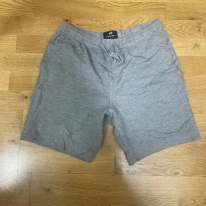 Grå shorts från H&M med snörning - Gråa midwaist shorts från H&M i regular fit. De har en mjuk bomullskänsla och elastisk midja med snörning för extra komfort. Perfekta för chill dagar eller när du vill ha något enkelt och stilrent. Klassisk design utan mönster eller extra detaljer.