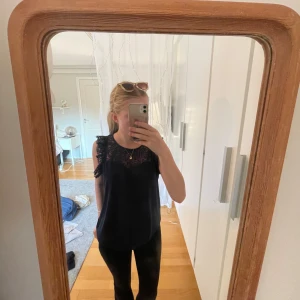 Marinblå spetsblus från Vero Moda - Supersnygg marinblå blus från Vero Moda med genombruten spets upptill och på axlarna. Ärmlös modell med rund halsringning och knapp i nacken. Perfekt att styla med jeans eller kjol för en trendig look. Storlek S men fungerar på större!