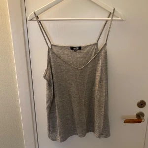 Grått linne från Bik Bok - Enkel och stilren grått linne från Bik Bok med smala axelband och v-ringning. Toppen är ärmlös och har en loose passform, perfekt för en chill och avslappnad look. Mjuk och skön i bomullsmix, passar till allt i garderoben.