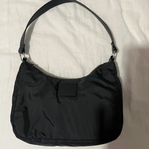 Svart axelväska från H&M - Snygg svart axelväska från H&M med stilren design. Materialet är lätt,litenoch smidigt, perfekt för att bära med sig det viktigaste.