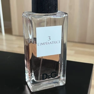 D&G L'Impératrice 3 EdT 100ml - D&G L'Impératrice 3 är en ikonisk parfym i en stilren, rektangulär glasflaska med svart kork. Doften är fräsch och fruktig, perfekt för dig som gillar en modern och feminin vibe. Flaskan rymmer 100 ml och har en ljusrosa vätska som syns genom det klara glaset. Skulle tippa på ca 60 ml kvar i flaskan