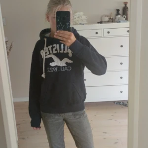 Mörkblå hoodie från Hollister - Mörkblå hoodie från Hollister med stor vit logga och text framtill. Tröjan har huva med vita snören och en klassisk känguruficka. Perfekt för dig som gillar en avslappnad och sportig stil. Den har inga defekter och är väldigt mjuk.💗 Skriv för funderingar❤️ storlek s