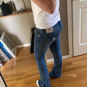 True Religion jeans bootcut - Säljer ett par blå jeans från True Religion med bootcut och snygga detaljer på bakfickorna. Jeansen har låg midja och är storlek 26. Säljer endast för att dem inte passar längre, älskar verkligen dessa byxor! Hål längst nere ( se bild) men absolut inget man ser när man har på sig dem🤗 