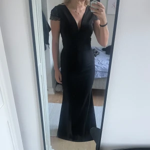 Svart långklänning med spetsdetaljer - Elegant svart långklänning från Girl Tall, köpt på Zalando, med djup v-ringning och fina spetsdetaljer på axlarna. Klänningen har figurnära passform och dragkedja i ryggen. Jag har endast använt den en gång. Om ni har frågor är det bara att skriva💕💕