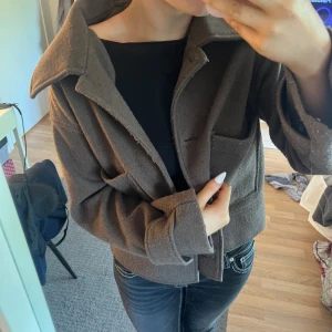 Brun kappa från Kappahl  - Säljer en brun overshirt från Kappahl i ullmix. Jackan har stora fickor framtill, bred krage och knappar vid ärmsluten. Saknas knappar där fram