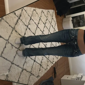 Rock Revival blå bootcut jeans - Snygga blå jeans från Rock Revival med bootcut passform och låg midja. Har knappast använt, men tyvärr så är det små fläckar på baksidan men inget som man märker. 