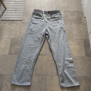 Grå mjukisbyxor från Corteiz , medium - Grå mjukisbyxor från GN med vit snörning i midjan och broderad logga på benet. Byxorna har raka ben, sidofickor och är gjorda i mjukt bomullsmaterial. Perfekta för chill dagar eller när du vill vara bekväm. Skulle rekommenderas till de som är 185cm uppåt 