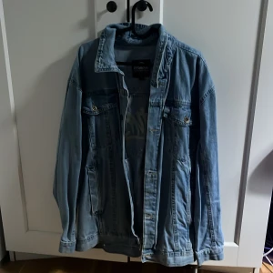 Ljusblå jeansjacka från Southpole - Snygg ljusblå jeansjacka från Southpole med stora tryck på ryggen. Klassisk modell med bröstfickor och knappar framtill. Jackan har en avslappnad passform och är perfekt för dig som gillar streetstyle. Materialet är slitstarkt denim och jackan har långa ärmar. Finns lite skavanker på ena sidan se sista bilden.