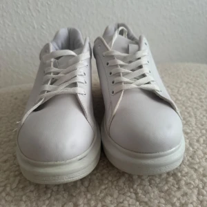 Vita sneakers från NLY Shoes strl 37 - Klassiska vita sneakers från NLY Shoes i storlek 37. Skorna har rund tå, snörning och en chunky platt sula. Tillverkade i syntetmaterial och polyester med bomull i fodret. Perfekta för en clean och stilren look. Använd en gång.