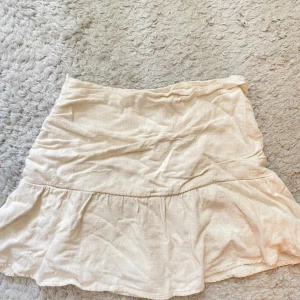 Beige volangkjol i linne - Supersöt beige kortkjol med volangkant och avslappnad passform. Kjolen är gjord i ett lätt linnematerial som känns luftigt och fräscht. Perfekt för varma dagar när du vill ha en enkel men ändå trendig look.