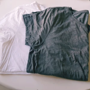2-pack H&M Basics t-shirts M - Två klassiska t-shirts från H&M Basics i storlek M. En är vit och den andra är grå, båda med rund hals och kort ärm. Perfekta för en clean och enkel stil. Tillverkade i mjuk bomull som känns skön mot huden.  Vit- helt skick dock obehandlade fläckar Grå- helt skick dock noppror