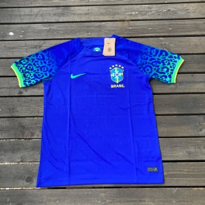 Blå Brasilien fotbollströja Nike M - Snygg blå Brasilien fotbollströja från Nike med CBF-emblem och fem stjärnor på bröstet. Ärmarna har leopardmönster i blått och grönt med gula detaljer. Tillverkad i Dri-Fit material som andas. Perfekt för dig som vill sticka ut på planen eller läktaren.