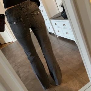 Grå bootcut jeans med fickdetaljer - Säljer ett par grå jeans med bootcut modell och snygga fickor med lock och knapp bak. Pris kan diskuteras vid snabb affär.