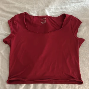 Röd croppad topp från SHEIN strl XL - Snygg röd croppad topp från SHEIN med korta ärmar och söt spetskant vid halsringningen. Toppen är tillverkad i stretchig polyesterblandning som sitter bekvämt och har en enkel, stilren design. Perfekt att matcha med jeans eller kjol för en trendig look.