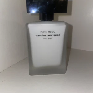 Narciso Rodriguez Pure Musc parfym - Stilren parfymflaska i frostat vitt glas med svart fyrkantigt lock. Pure Musc for her från Narciso Rodriguez har en minimalistisk design och känns lyxig och modern. Perfekt för dig som gillar eleganta och enkla detaljer.