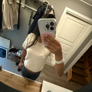 Vit stickad topp Holly & Whyte - Superfin vit stickad topp från Holly & Whyte by Lindex. Kortärmad och croppad modell med två stora guldknappar på axeln som snygg detalj. Mjuk struktur och rund halsringning, perfekt till jeans eller kjol för en trendig look. (Köpt för 500kr)