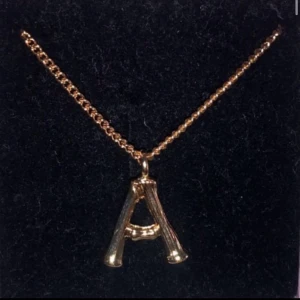 Guldigt halsband med olika bokstäver - Snyggt halsband i guldton med ett hängsmycke format som bokstaven A. Kedjan är tunn och glänsande, och bokstaven har en cool, lite rustik design som sticker ut. Perfekt accessoar för dig som vill bära din initial.