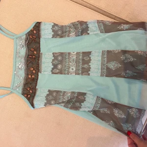 Turkos mönstrad linnetopp med broderi - Supersöt turkos linnetopp med tunna axelband och transparenta partier. Toppen har bruna och vita mönsterdetaljer samt broderade blommor och paljetter upptill. Perfekt för varma dagar när du vill sticka ut lite extra.