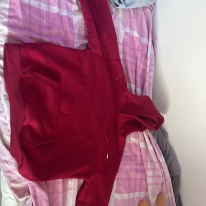 Röd hoodie med huva och ficka storlek M - Säljer en snygg röd hoodie med huva och dragsko. Tröjan har en stor magficka och långa ärmar med muddar. Perfekt för dig som gillar en enkel och stilren look. Materialet känns mjukt och skönt mot huden.